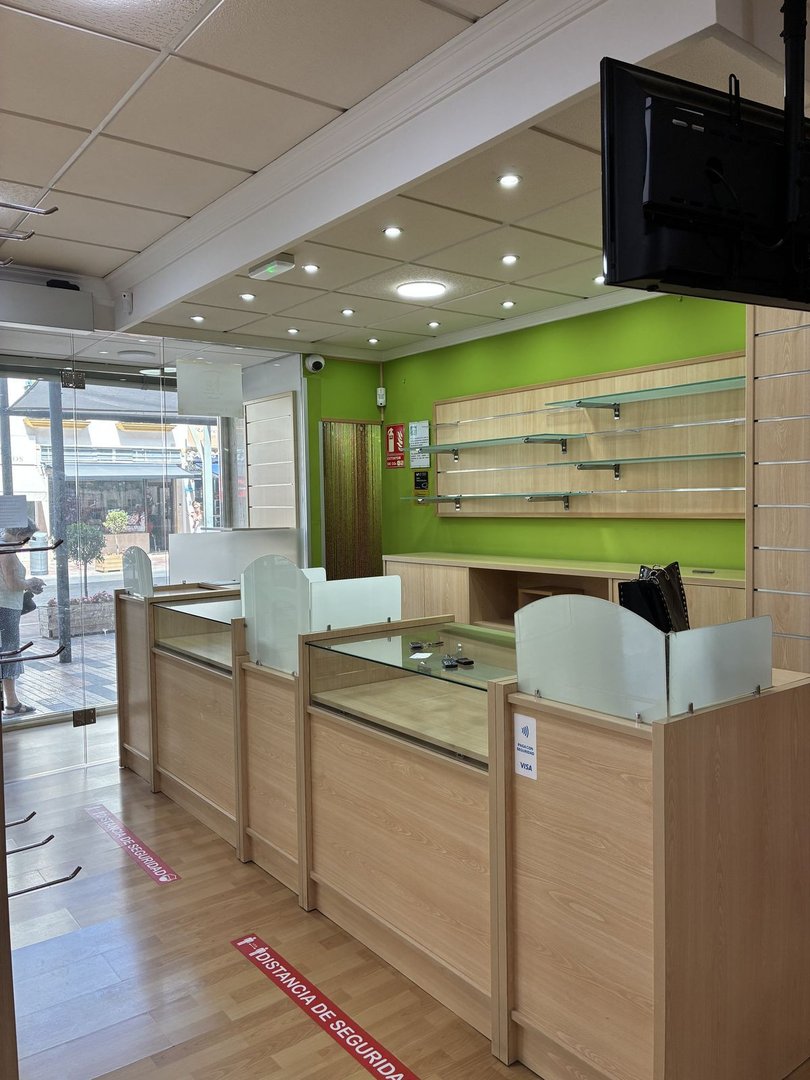 Interior view of a commercial space with light wood display counters, glass partitions, and green walls with shelves.