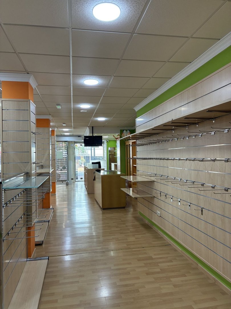 Empty retail store interior with wooden floors, shelving units, counters, and bright overhead lighting.