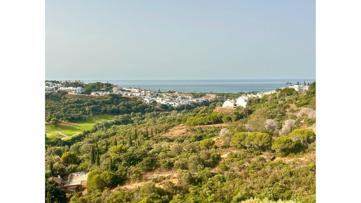 Scenic view of white villas nestled among green hills, overlooking the golf course and the distant blue sea.