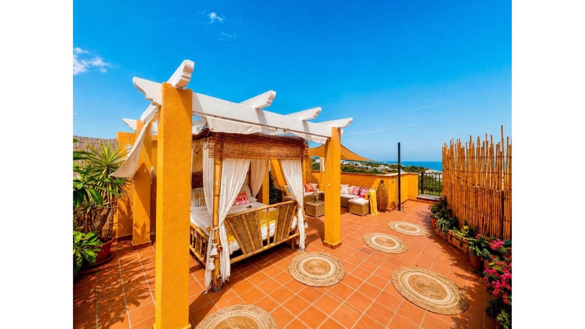 Terrace with a daybed, lounge seating, round rugs, and a sea view under a clear blue sky.