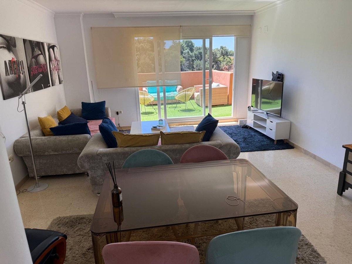 Modern living room with comfortable sofas and a large window overlooking a sunny terrace with a swimming pool and lounge chairs.