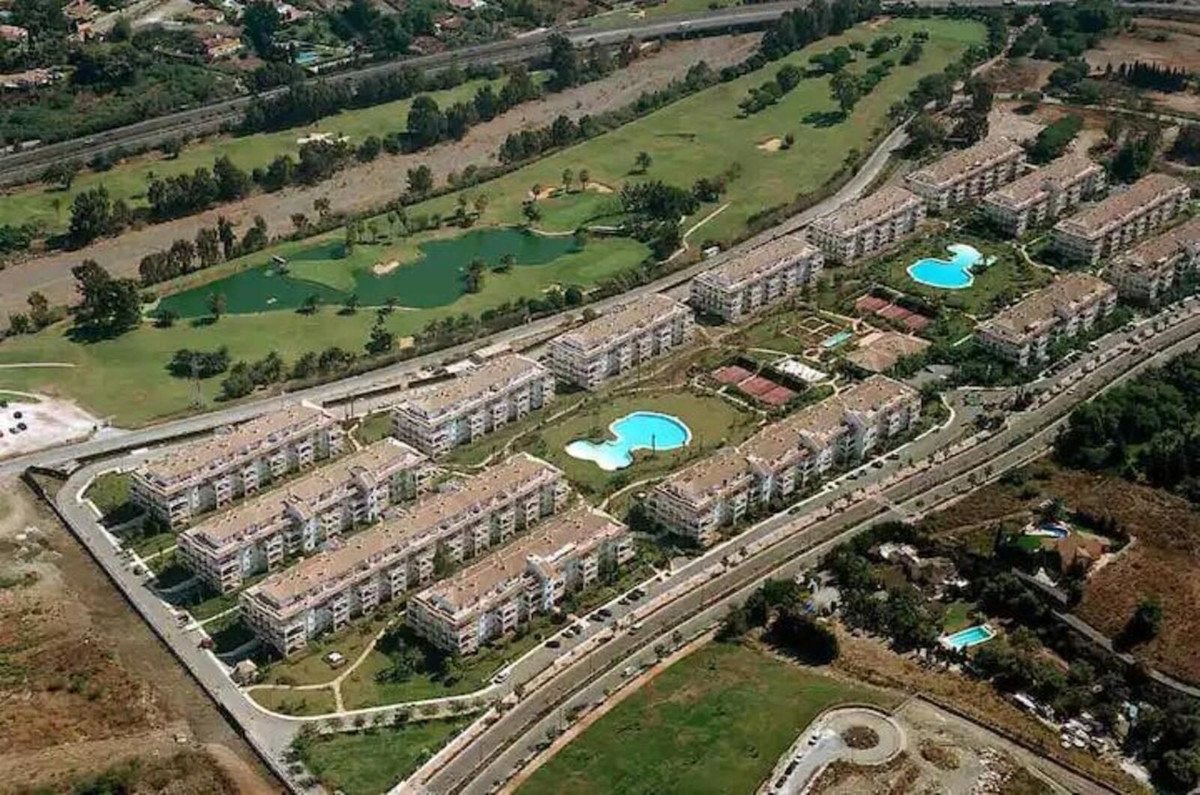 Aerial view of modern apartment buildings in a resort complex with a golf course, swimming pool, and tennis courts.