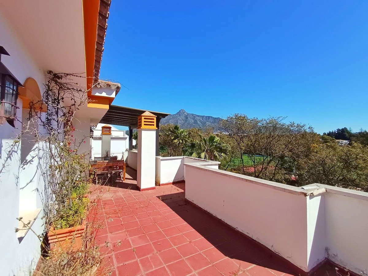 A spacious terrace with outdoor dining furniture and a distant mountain view under a clear blue sky.
