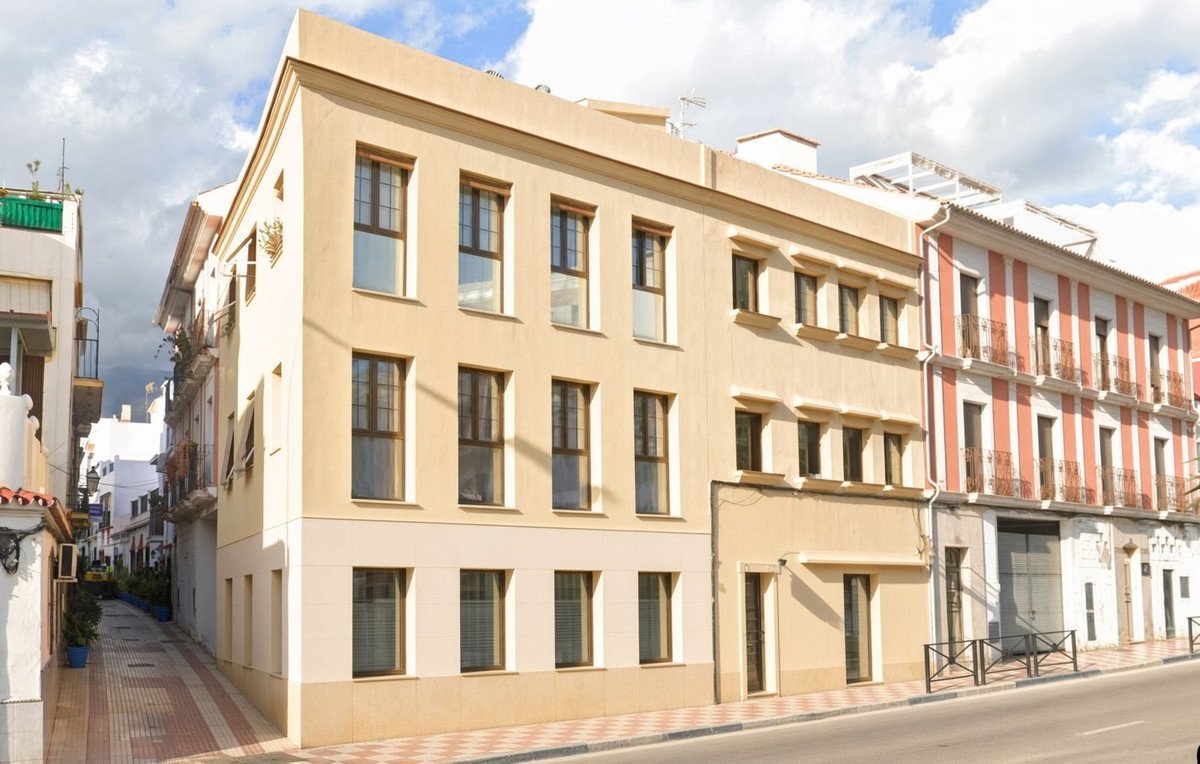 A neutral-toned building facade with multiple windows, on a street with a red and white striped building next door.