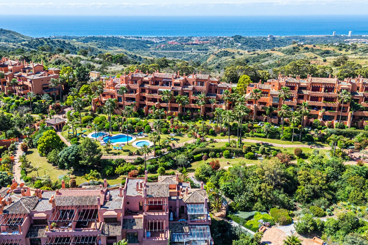 Aerial view of a luxury resort with terracotta buildings, palm trees, pools, and ocean views.