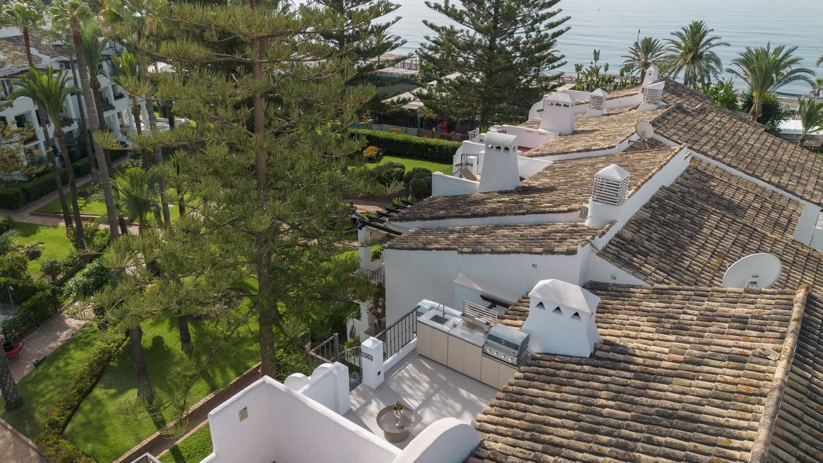 Rooftop terrace with an outdoor kitchen, overlooking a garden and the sea in the distance.