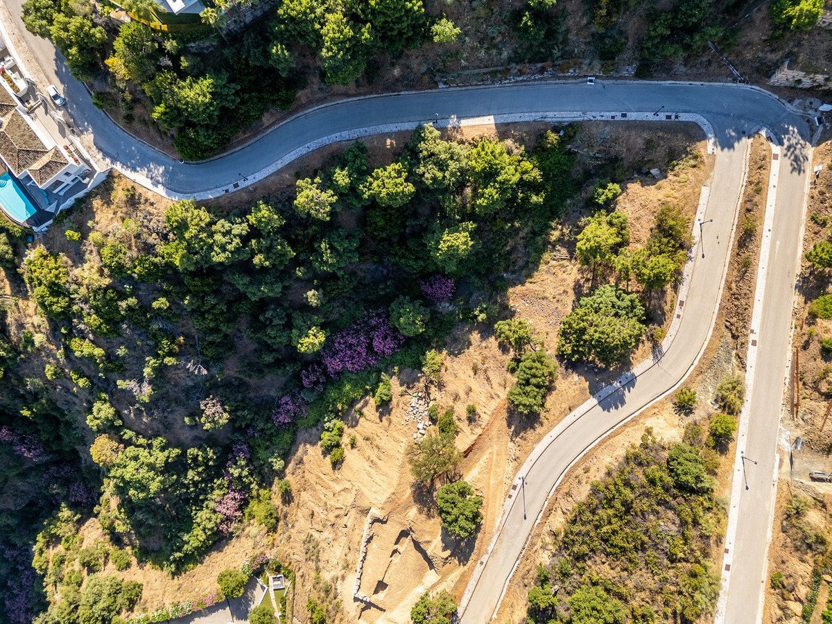 Aerial view of a hillside property with winding roads, lush greenery, and a swimming pool visible near a modern villa.