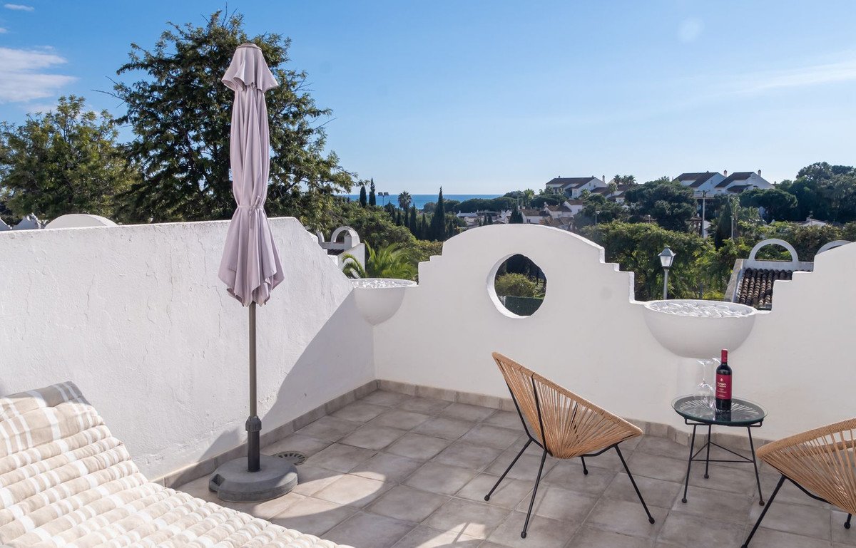 Terrace with lounge chairs, small table with wine, and a distant sea view under a clear blue sky.