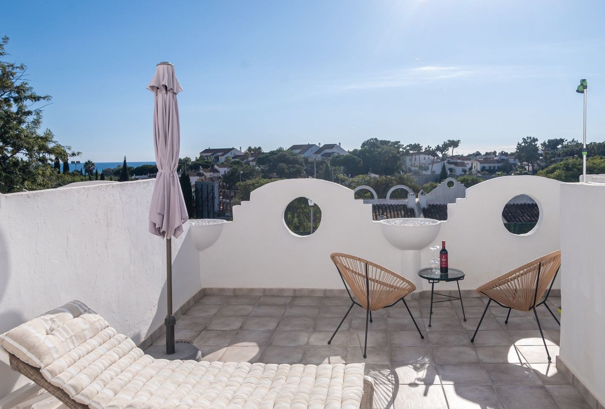 Terrace with lounge chairs, table, wine, umbrella, and a distant sea view under a clear blue sky.