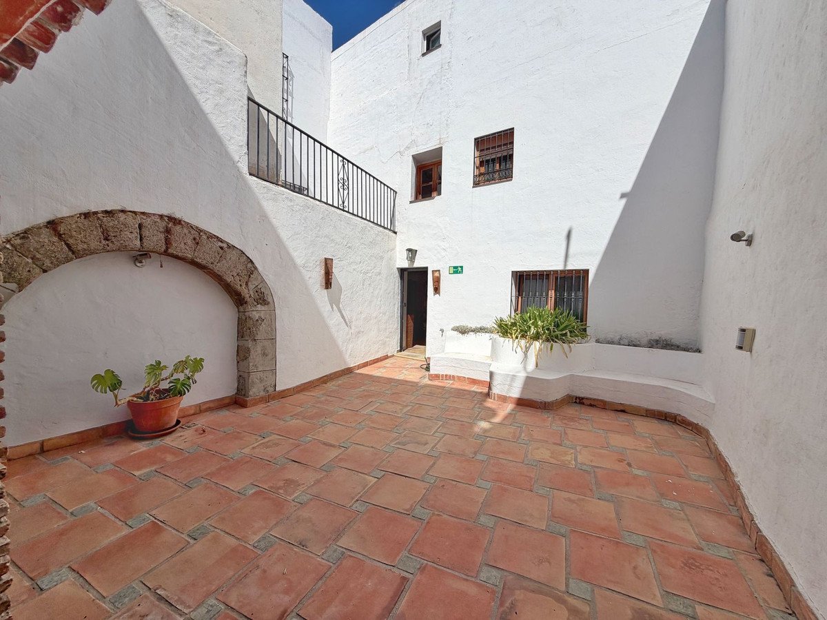 Terracotta tiled courtyard with white walls, arched alcove, potted plant, and a built-in planter with greenery.