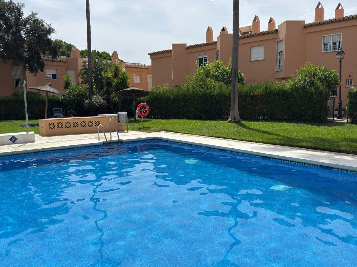 Communal swimming pool in front of apartment buildings, surrounded by green grass and trees.