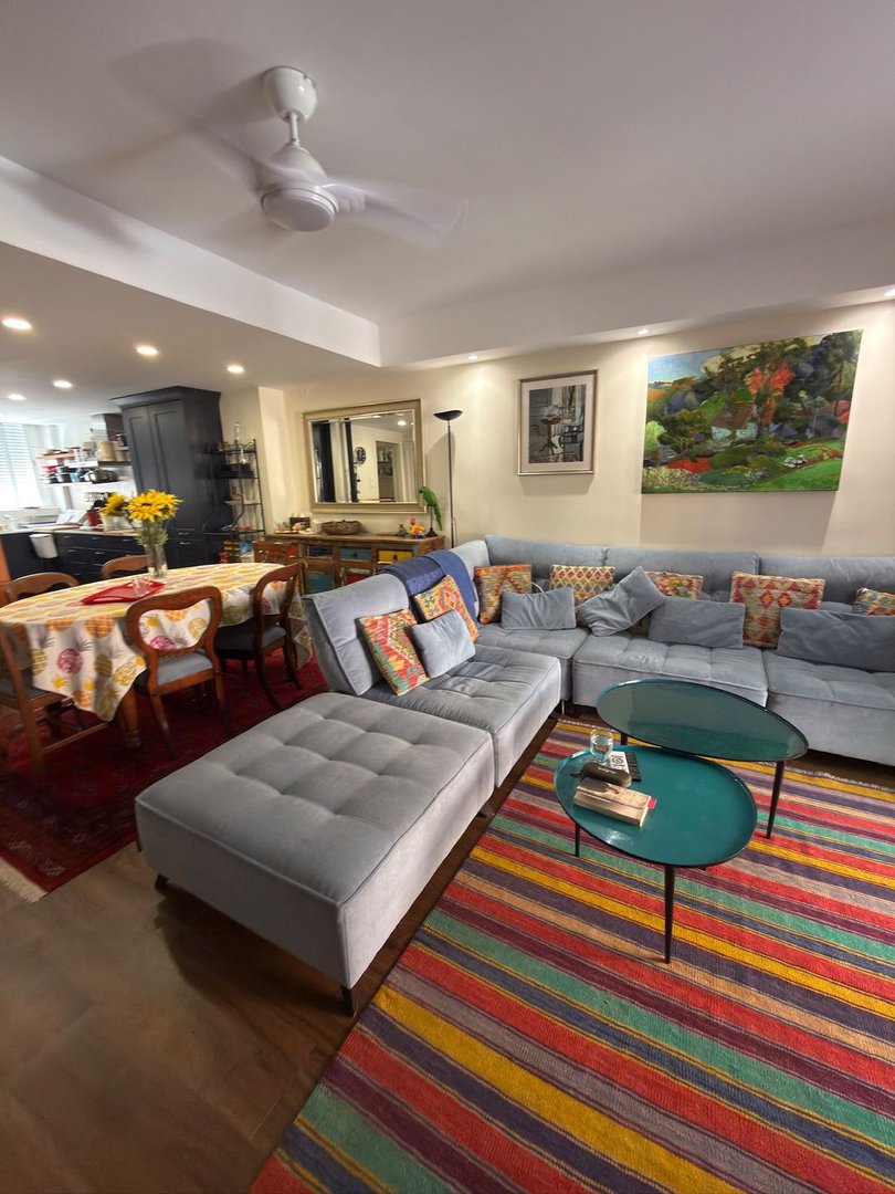 A spacious living and dining area features a blue sectional sofa, colorful striped rug, and a dining table with chairs.