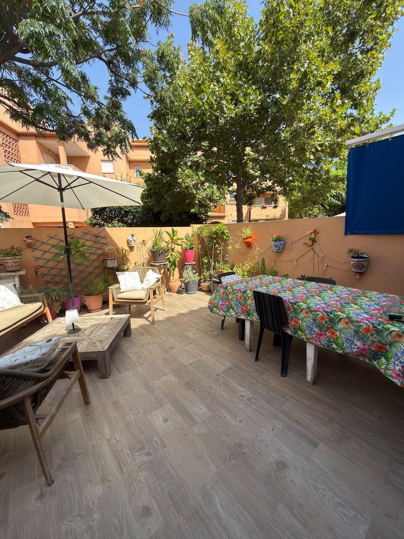 A spacious terrace with wooden flooring, featuring outdoor seating, a large dining table, plants, and an umbrella.