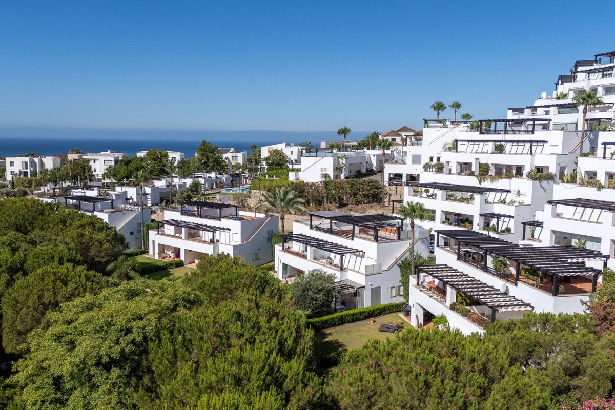 Modern white apartments with terraces and pergolas, overlooking the sea and lush greenery.