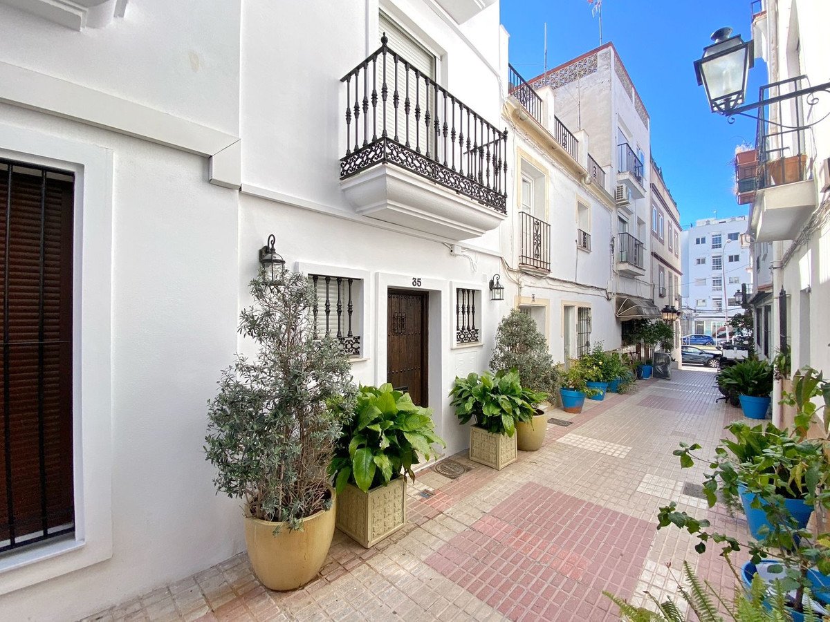 White stone pavement with potted plants and a balcony overlooking a narrow street