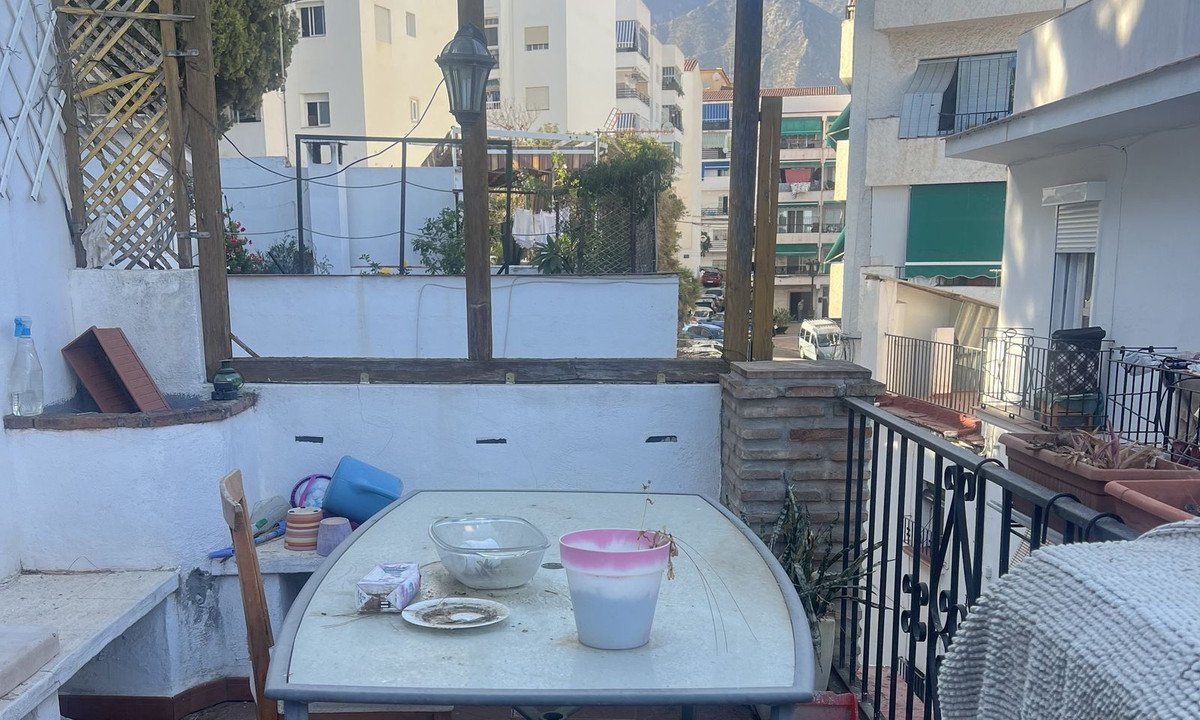 Balcony with table, chairs, and potted plants, overlooking residential buildings and mountains.