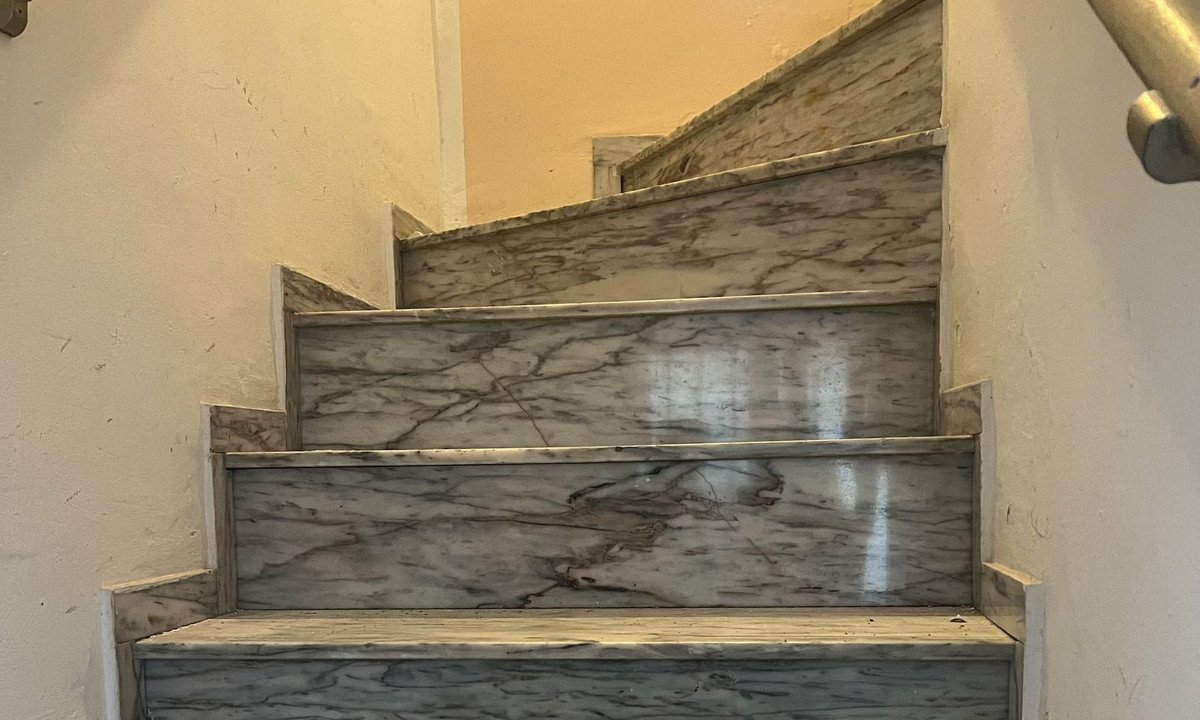 Marble staircase with gray veining, white walls, and metal handrail in a residential interior.