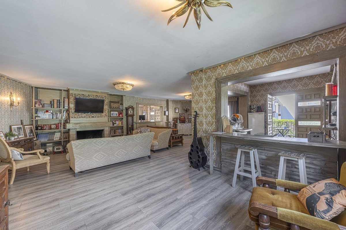 Spacious living room with patterned wallpaper, fireplace, built-in bookshelves, a bar area, and an outdoor view.