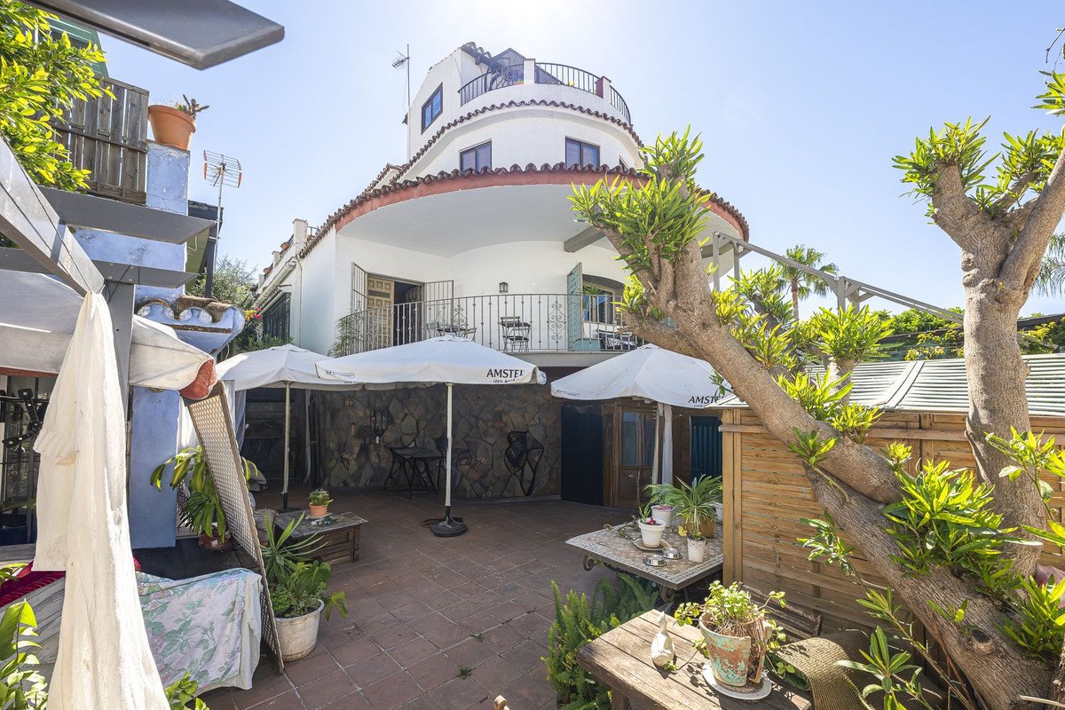Terrace with white umbrellas, potted plants, and a curved white building with balconies and a tower in the background.