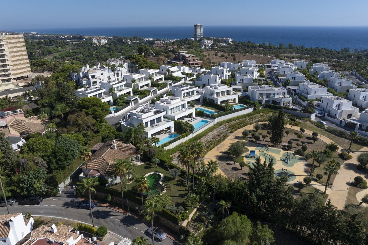 Aerial view of modern white villas with private pools, overlooking the sea and a landscaped park.