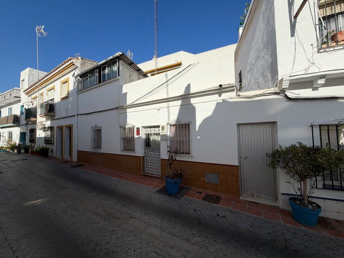 Exterior view of a white townhouse on a street, featuring balconies, windows, and a metal garage door.