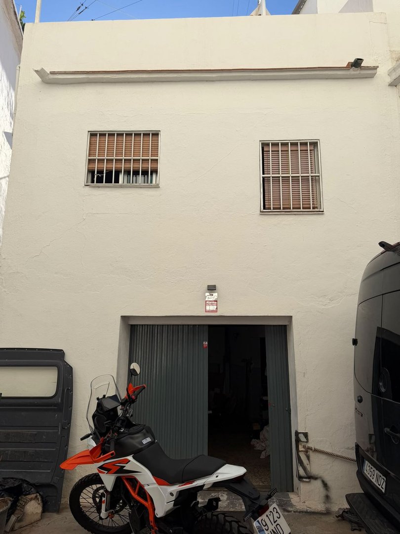 Exterior of a white building with barred windows and a large double door, featuring a motorcycle and van parked outside.