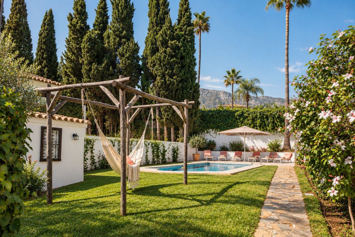Sunny garden with swimming pool, hammock, lounge chairs, and a mountain view in the background.