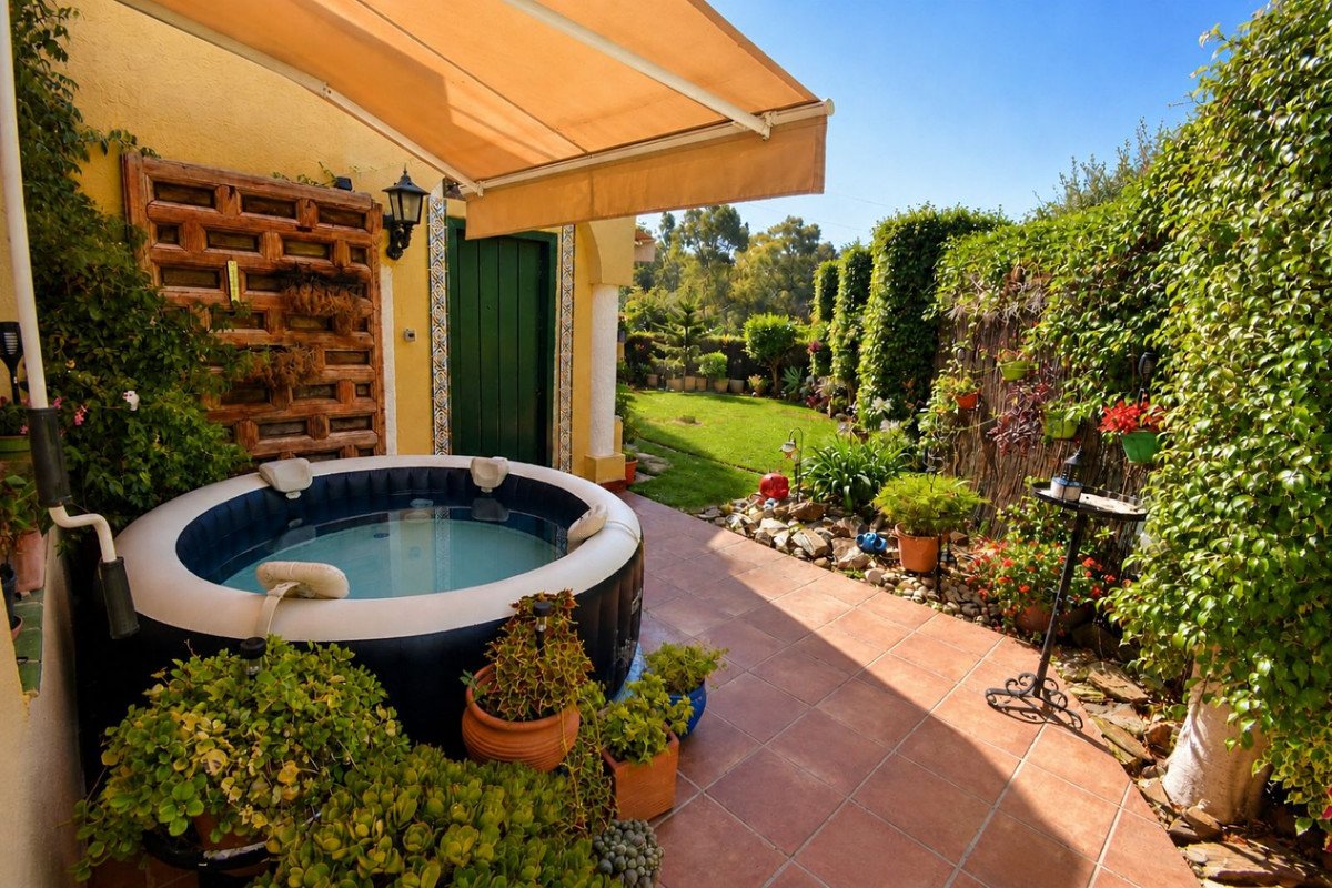 An inflatable hot tub sits on a tiled patio beside a lush green garden, under an awning.