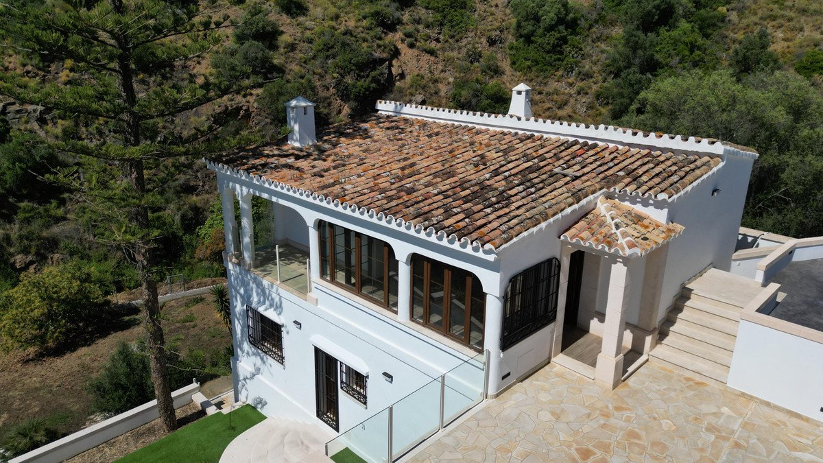 White villa with terracotta roof, glass railings, and mountain views.