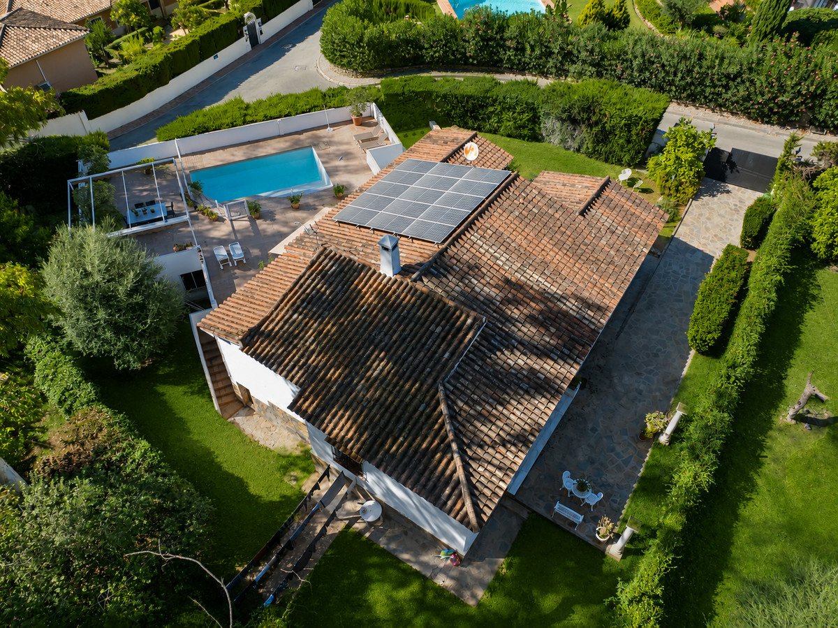 Aerial view of a house with a swimming pool, solar panels, and lush green garden