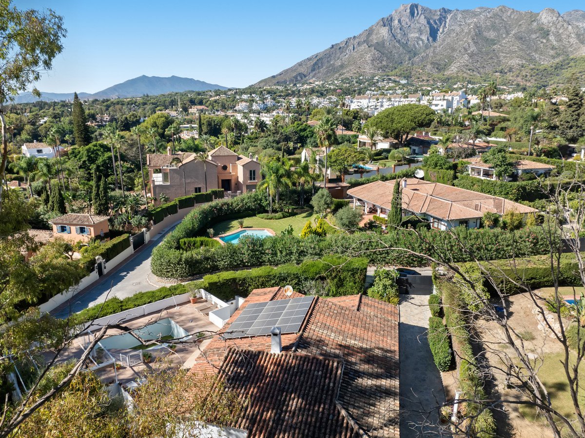 Aerial view of a villa with pool, solar panels, and mountain backdrop.