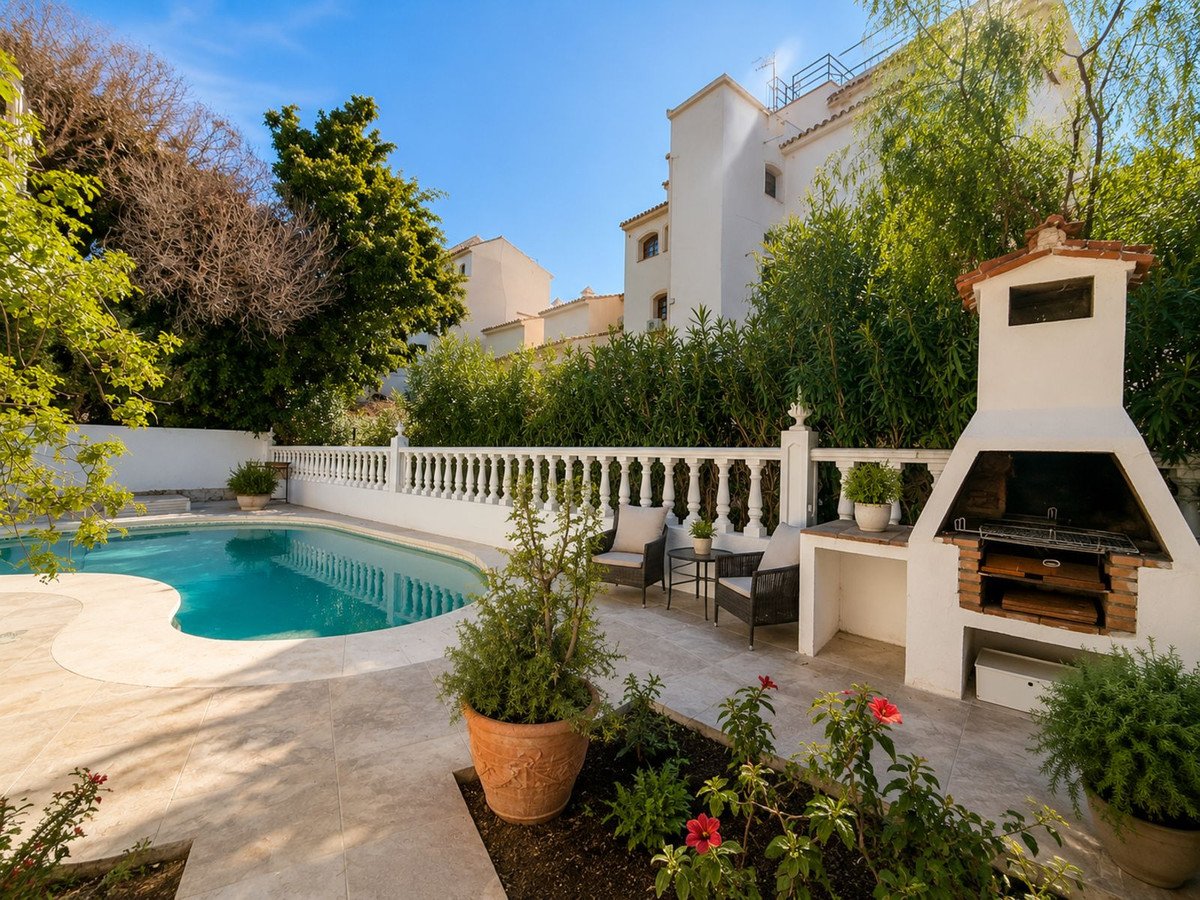 A swimming pool and built-in BBQ area with seating, surrounded by lush greenery and a white balustrade.