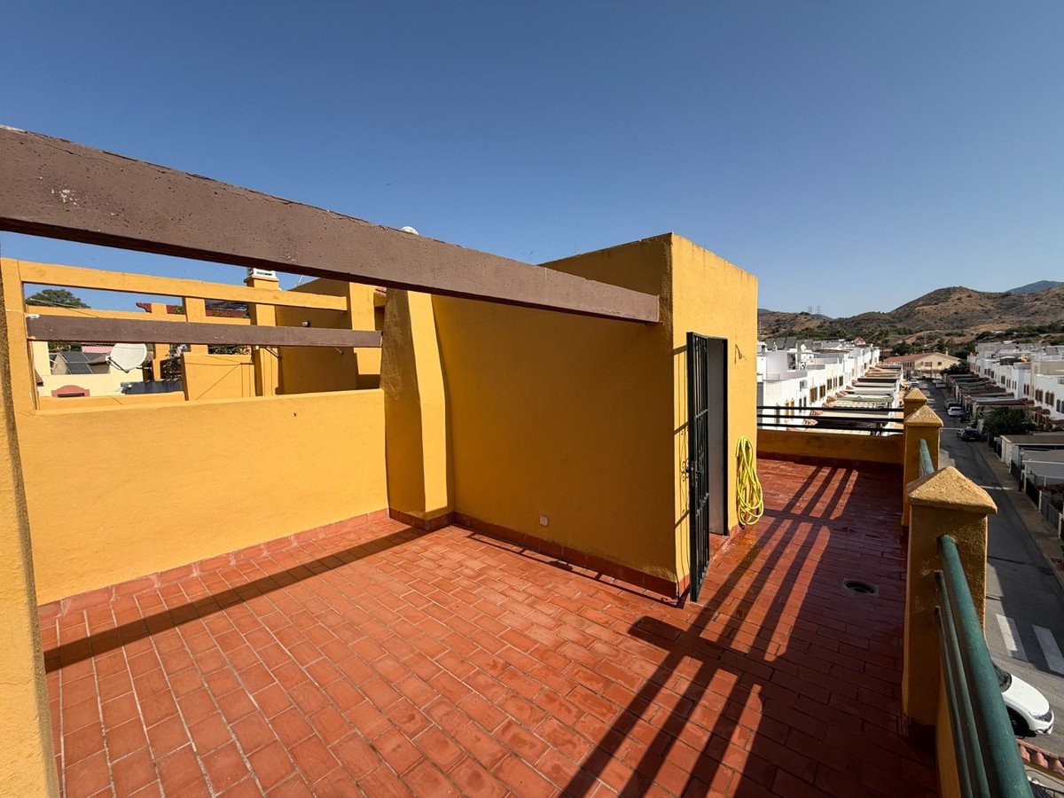 Sunny terrace with terracotta tiles, yellow walls, and a view of a residential area and hills.