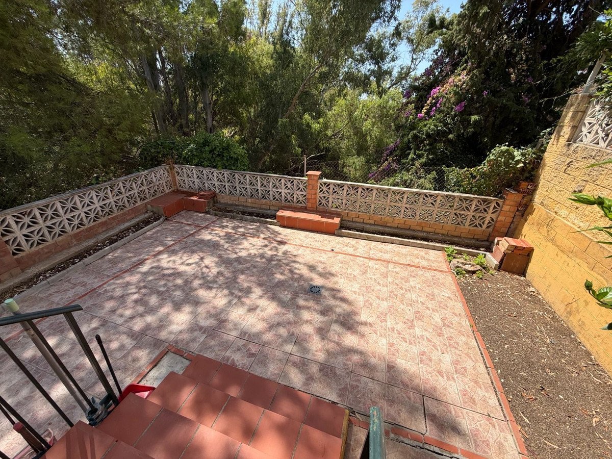 A tiled patio area with decorative concrete block walls and steps, surrounded by lush greenery and trees.
