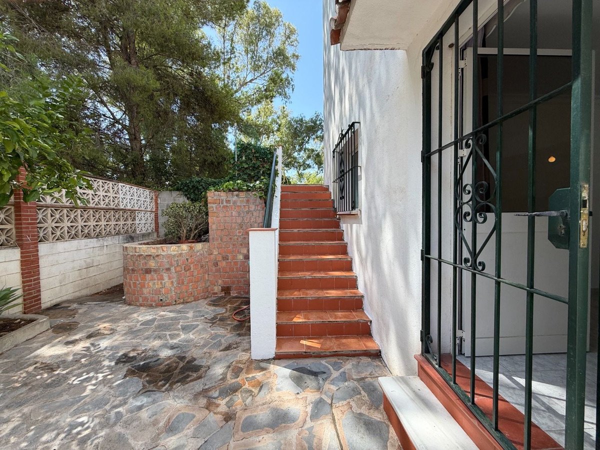 Outdoor paved terrace with decorative brick planter, red tiled steps, and a green metal gate leading to the house.