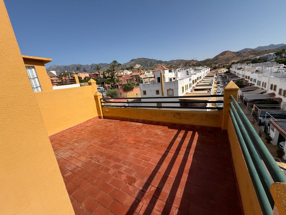 Terrace with red tiles offering a view of a town and distant mountains under a clear blue sky.
