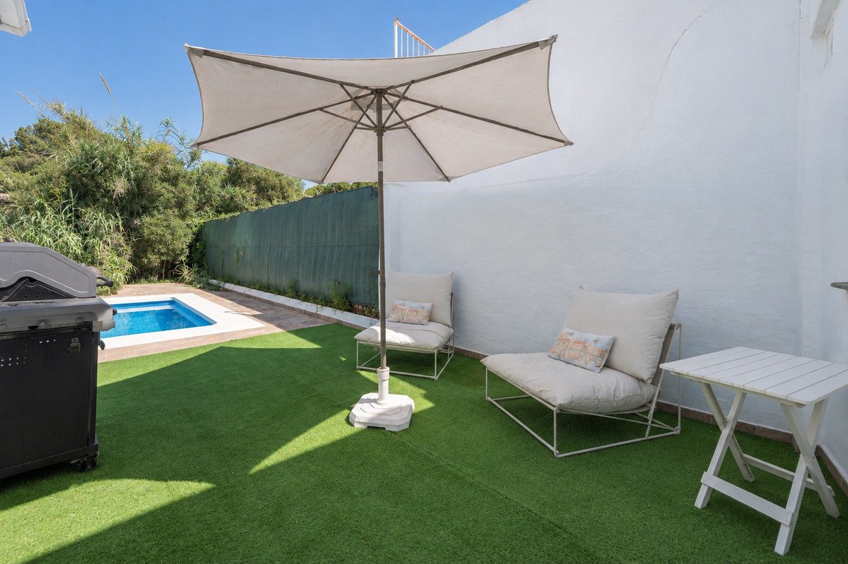 Outdoor patio with a small swimming pool, BBQ grill, chairs, and umbrella on a sunny day.
