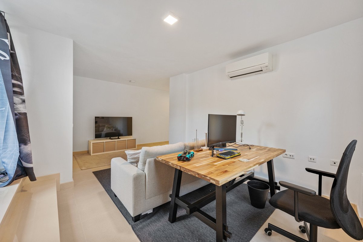 A modern living area featuring a sofa, desk with a computer, and a television, with air conditioning unit visible on the wall.