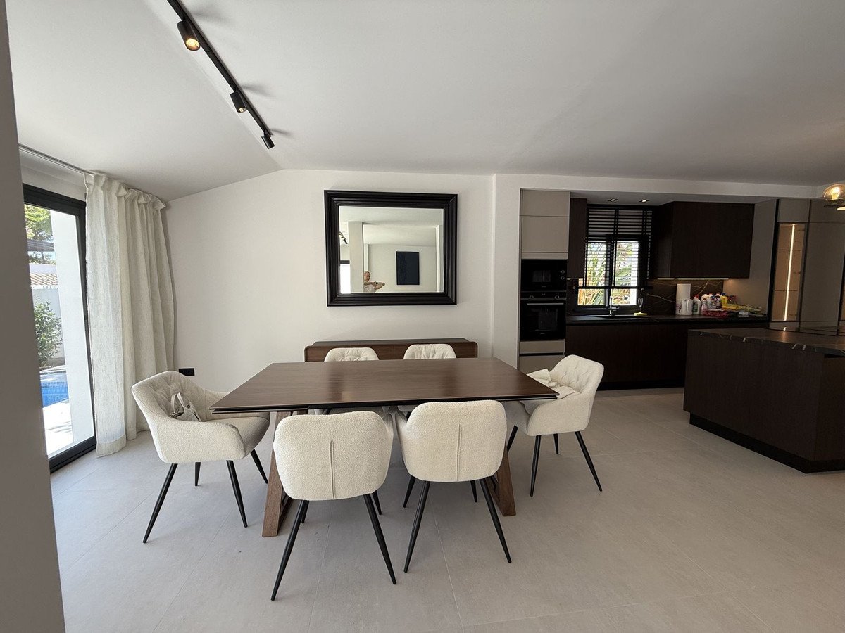 Modern dining area with wooden table, white chairs, and kitchen in background.