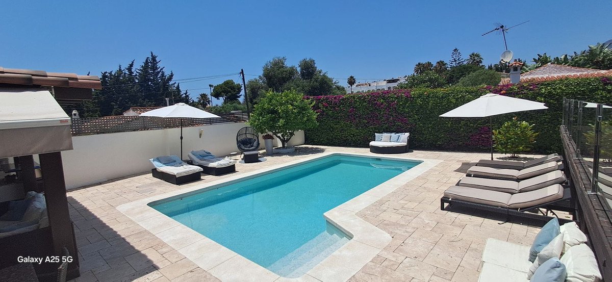 Private pool area with lounge chairs, umbrellas, and lush greenery under a clear blue sky.