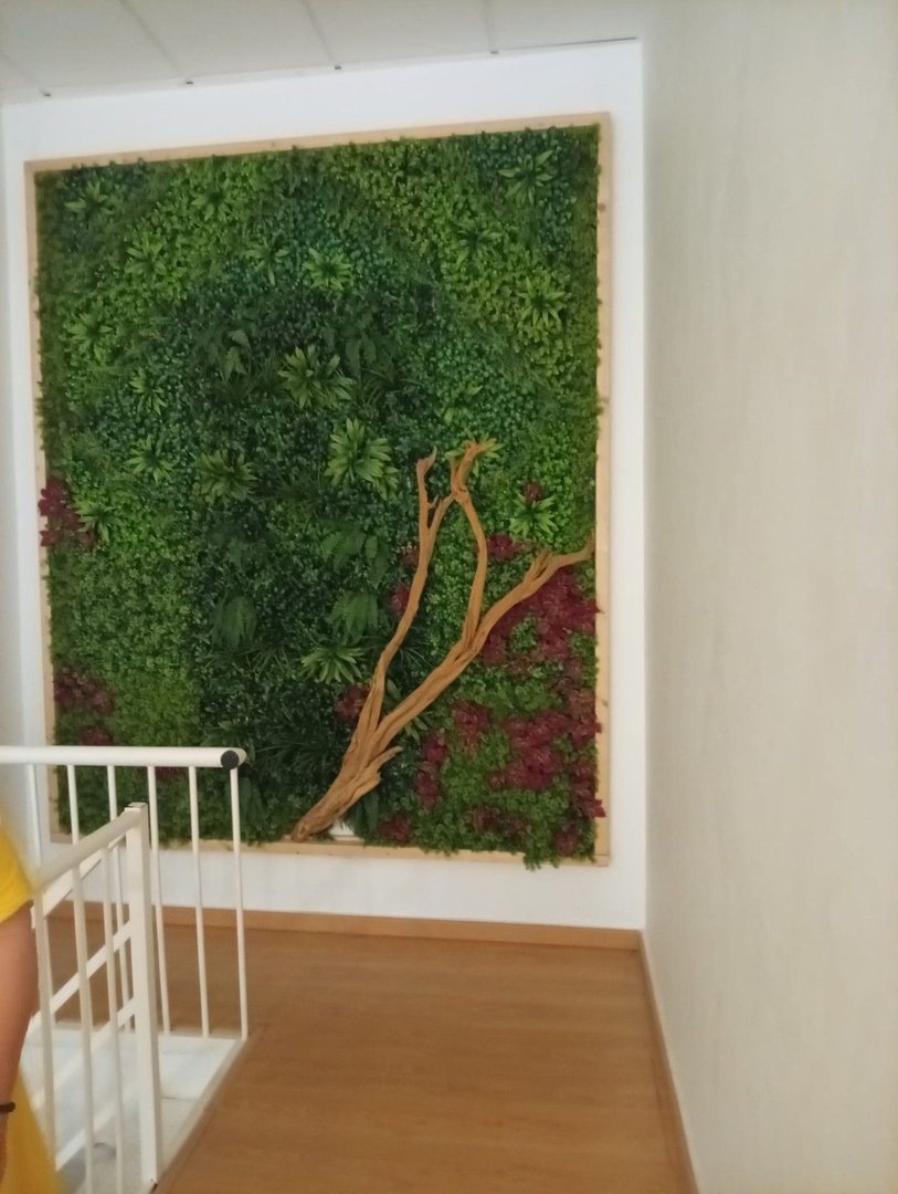 A vibrant green living wall with a decorative driftwood branch and red flowers, framed in wood.