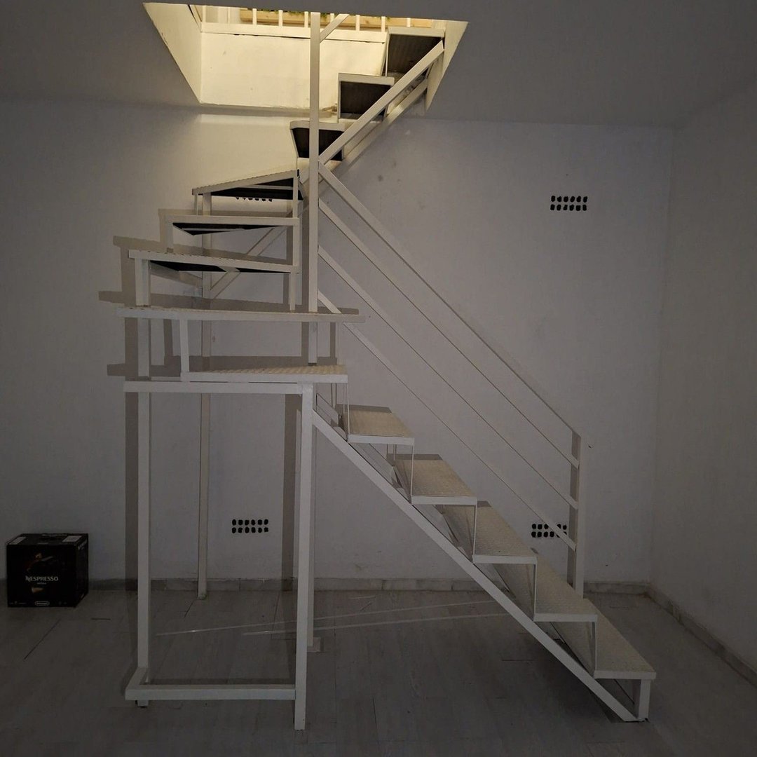 A white metal spiral staircase with modern design, leading up to a bright opening in the ceiling.