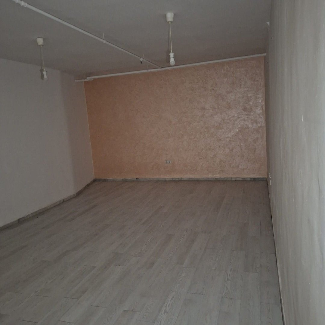 An empty room with light wood flooring and a textured peach accent wall. Bare light bulbs hang from the ceiling.