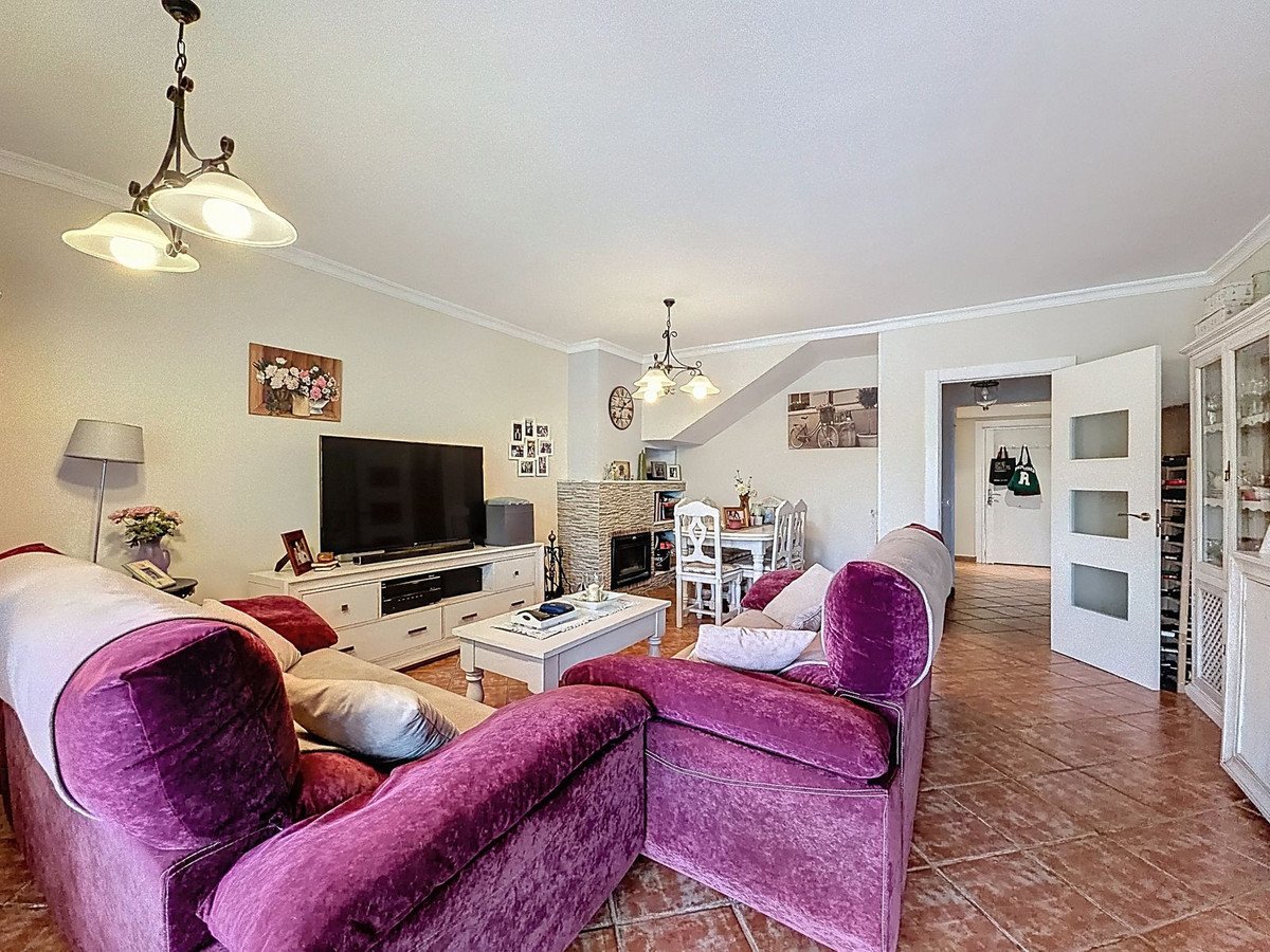 Spacious living and dining room with comfortable purple sofas, fireplace, and dining table, leading to a hallway.