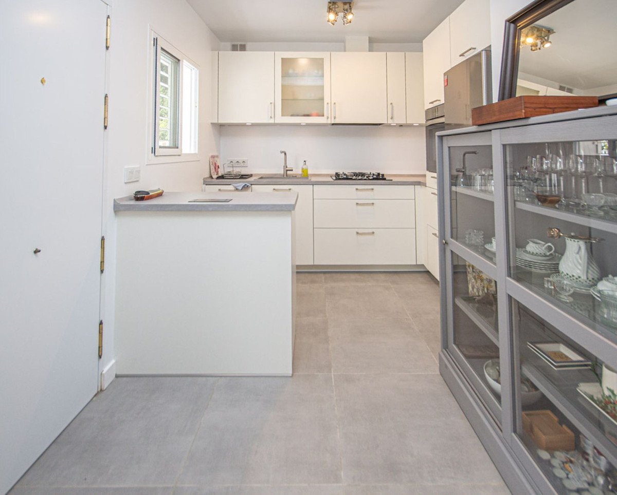 Modern kitchen with white cabinets, a breakfast bar, and a display cabinet filled with dishes.