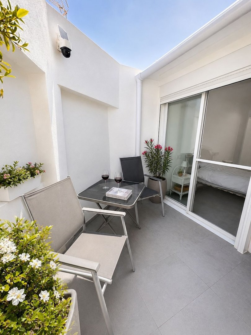 A balcony with a table, chairs, and potted plants near a sliding glass door.
