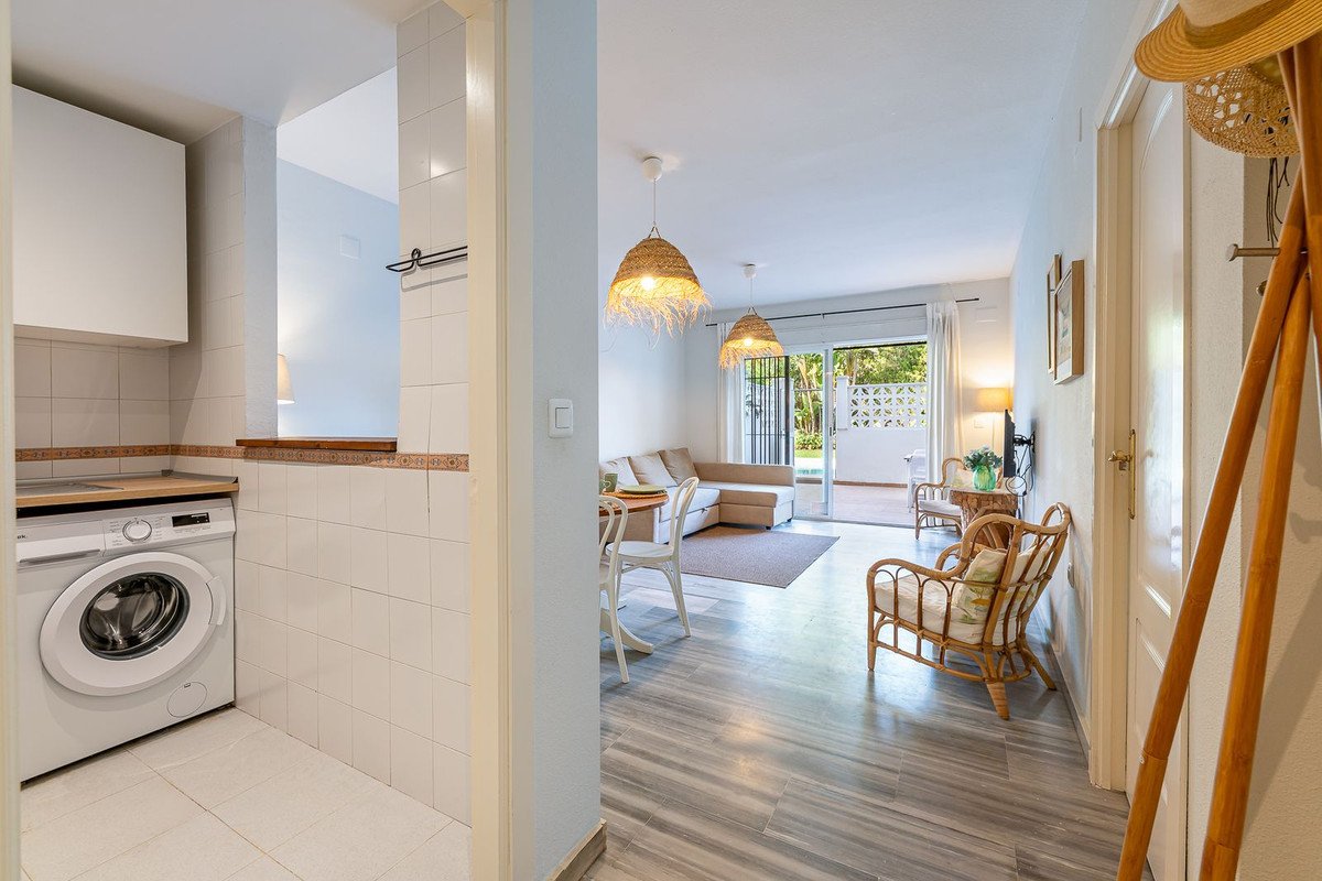 A bright living room with a kitchenette, sofa, and access to a sunny terrace overlooking greenery.