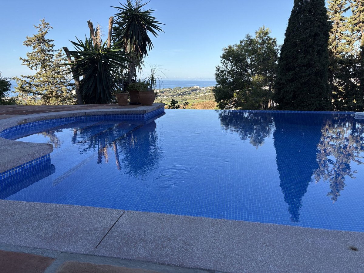 Infinity pool with blue tiled water and a scenic view of the sea and distant hills.