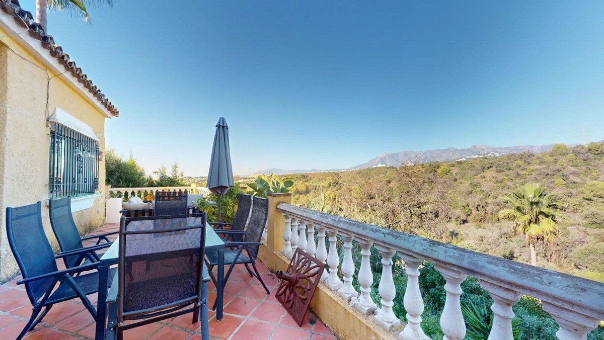 Terrace with outdoor seating and umbrella, overlooking a scenic mountain landscape under a clear blue sky.