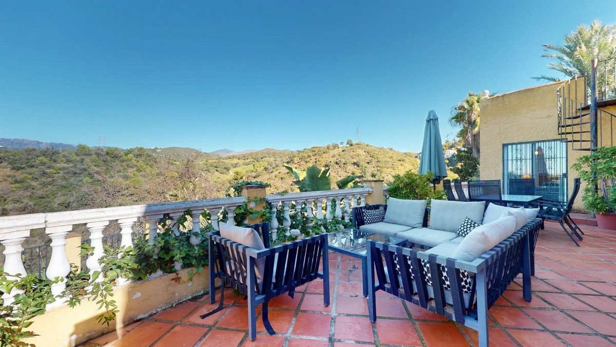 Terrace with outdoor seating, coffee table, and a spiral staircase leading to the house, offering a beautiful hill view.